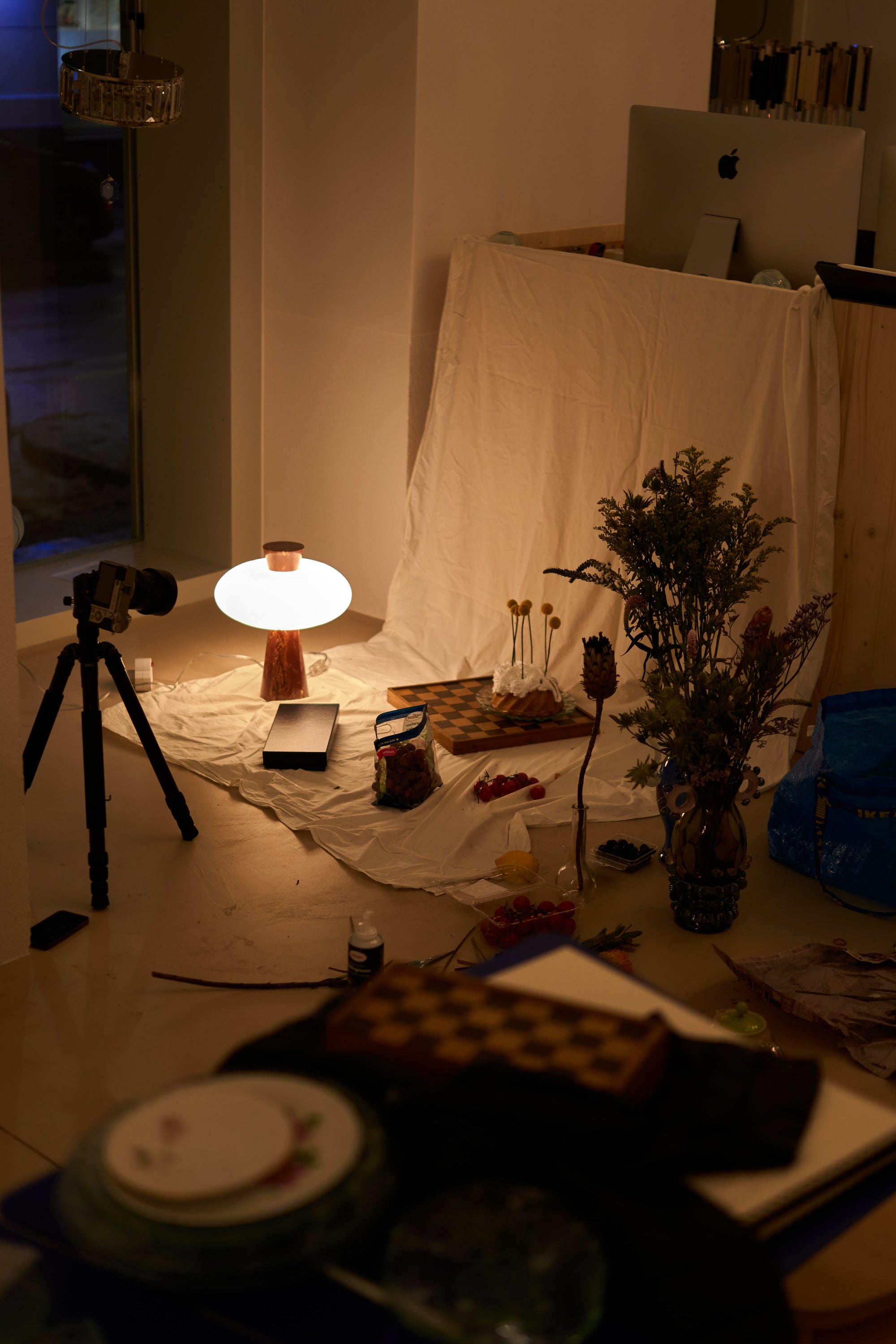 Dark room with a camera on a tripod, light bulb, and various items on a table.