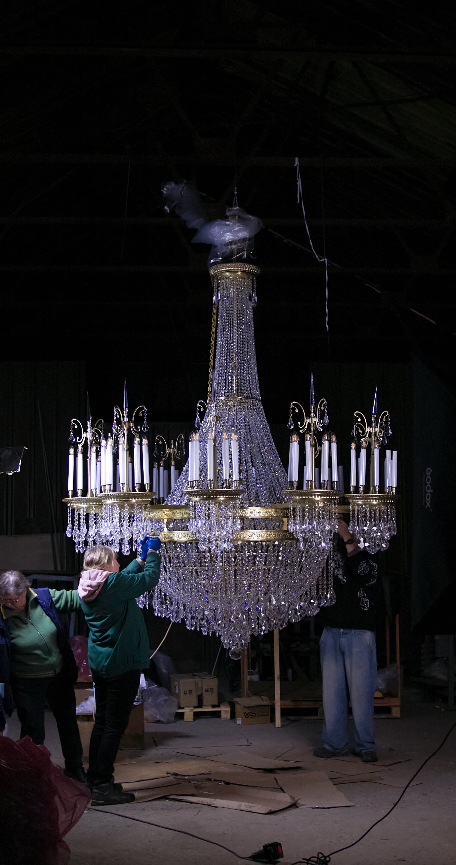 Craftspeople checking a large ZAVADSKI crystal chandelier with garlands and candle bulbs in the workshop